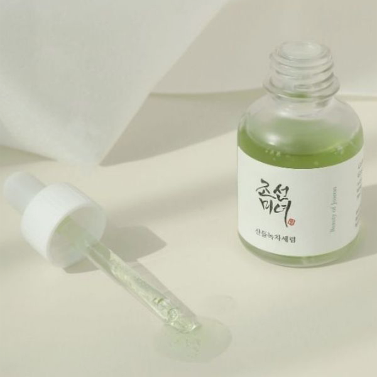 Durchsichtige Tropfflasche mit dem „Beauty of Joseon Calming Serum: Grüner Tee + Panthenol“, daneben ein Tropfer auf einem hellen Untergrund.