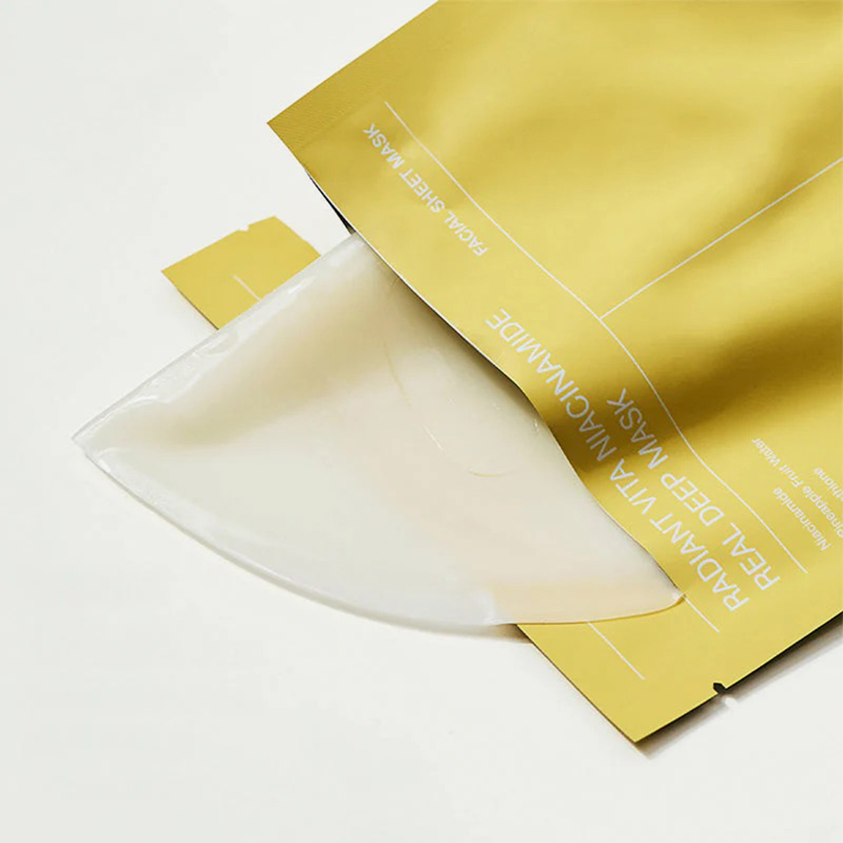 Eine gelbe Biodance Radiant Vita Niacinamide Real Deep Mask-Verpackung, aus der eine durchscheinende Maske herausgleitet.