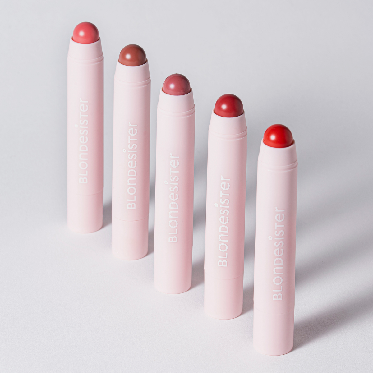 Fünf rosa „2 IN 1 IT’S UP TO YOU LIP OR CHEEK“-Tuben von BLONDESISTER stehen aufrecht da und zeigen jeweils einen einzigartigen Farbton.