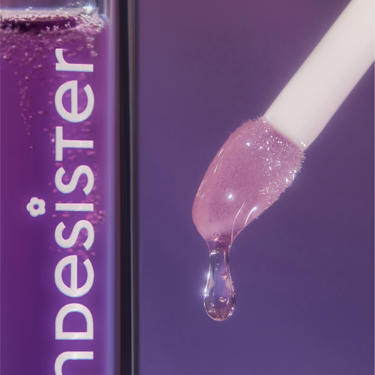 Eine Nahaufnahme des Applikators des BLONDESISTER 3 IN 1 CUTE LIPPY LIP OIL, von dem violetter Lipgloss herabtropft, neben der violetten Tube.