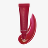 Eine Tube „Danessa Myricks Beauty Glosswork 4D Ultra Shine Plumping Gloss“ mit rotem Gloss, daneben auf weißem Hintergrund aufgetragen.