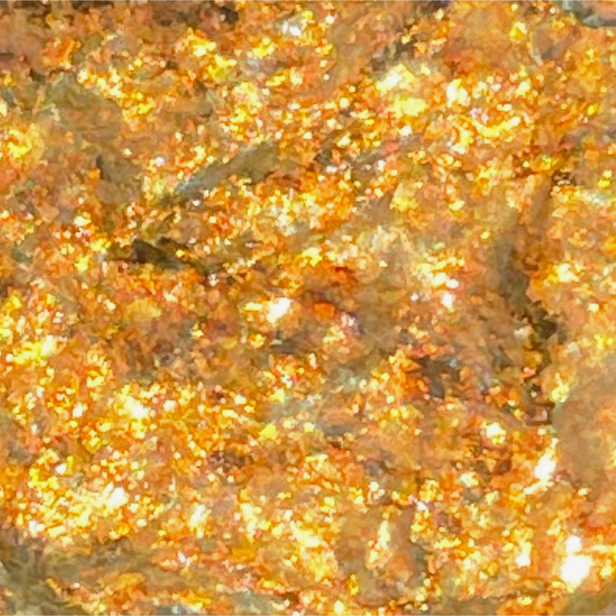 Die Nahaufnahme von Danessa Myricks Beauty Infinite Chrome Flakes Fire Ball zeigt eine glitzernde Oberfläche mit funkelnden goldenen und orangen Flecken, die das Licht reflektieren.
