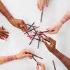 Sechs Hände mit unterschiedlichen Hauttönen halten Essence 8h Matte Comfort Lipliner über einem weißen Tisch und zeigen Farbmuster auf ihren Armen.