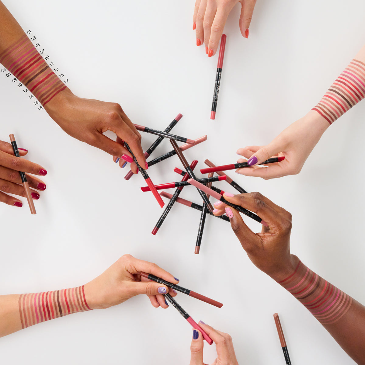 Sechs Hände mit unterschiedlichen Hauttönen halten Essence 8h Matte Comfort Lipliner über einem weißen Tisch und zeigen Farbmuster auf ihren Armen.