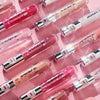 Diagonale Reihen von Essence Extreme Shine Volume Lipgloss-Tuben in Rosa- und Nude-Tönen auf einem rosa Hintergrund.