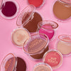 Essence soft TOUCH BOUNCY BLUSH compacts in verschiedenen Farbtönen werden auf einem rosa Hintergrund präsentiert.