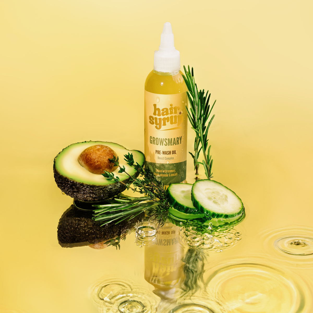 Growsmary Haaröl von Hair Syrup mit Avocado, Gurkenscheiben und Rosmarinzweigen auf einem leuchtend gelben Hintergrund mit Wasserkräuseln.
