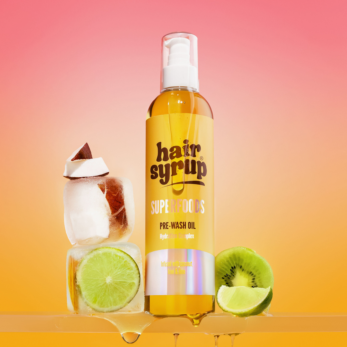 Flasche Hair Syrup Superfoods Pre-Wash Oil vor warmem Farbverlauf; daneben Eiswürfel mit Limette und Kokos sowie eine halbe Kiwi.