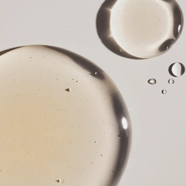Transparente Serum-Tropfen mit leicht gelblichem Ton auf hellem Hintergrund, flüssige Textur in Nahaufnahme.