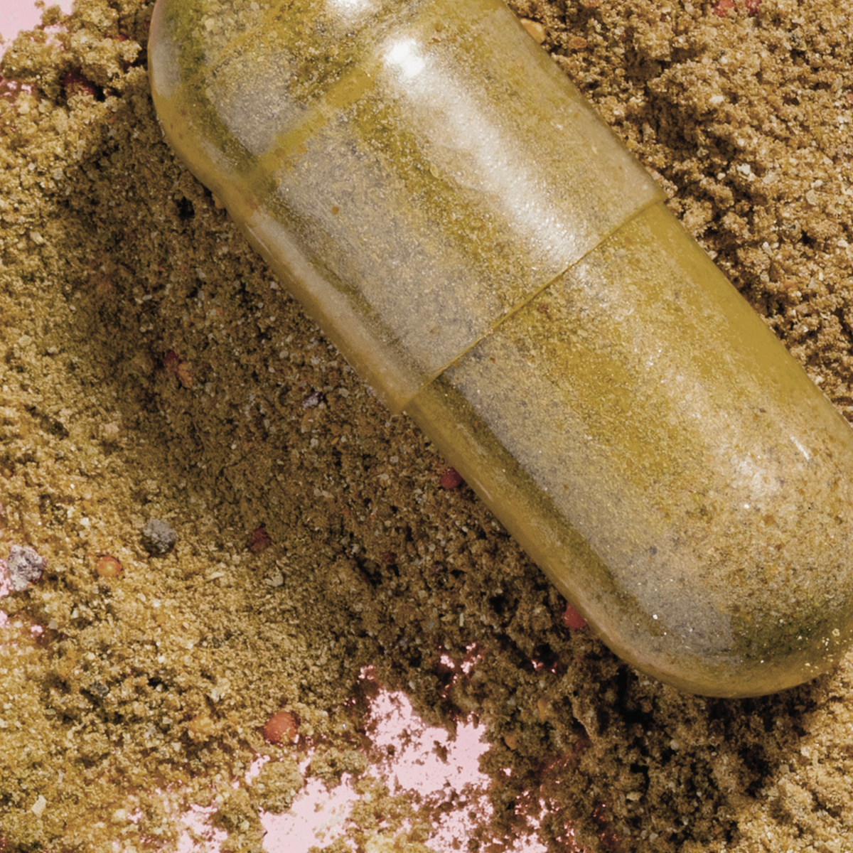 Nahaufnahme einer transparenten SKINtamin Kapsel mit pflanzlichem Pulver, liegend auf körnigem, goldbraunem Hintergrund.