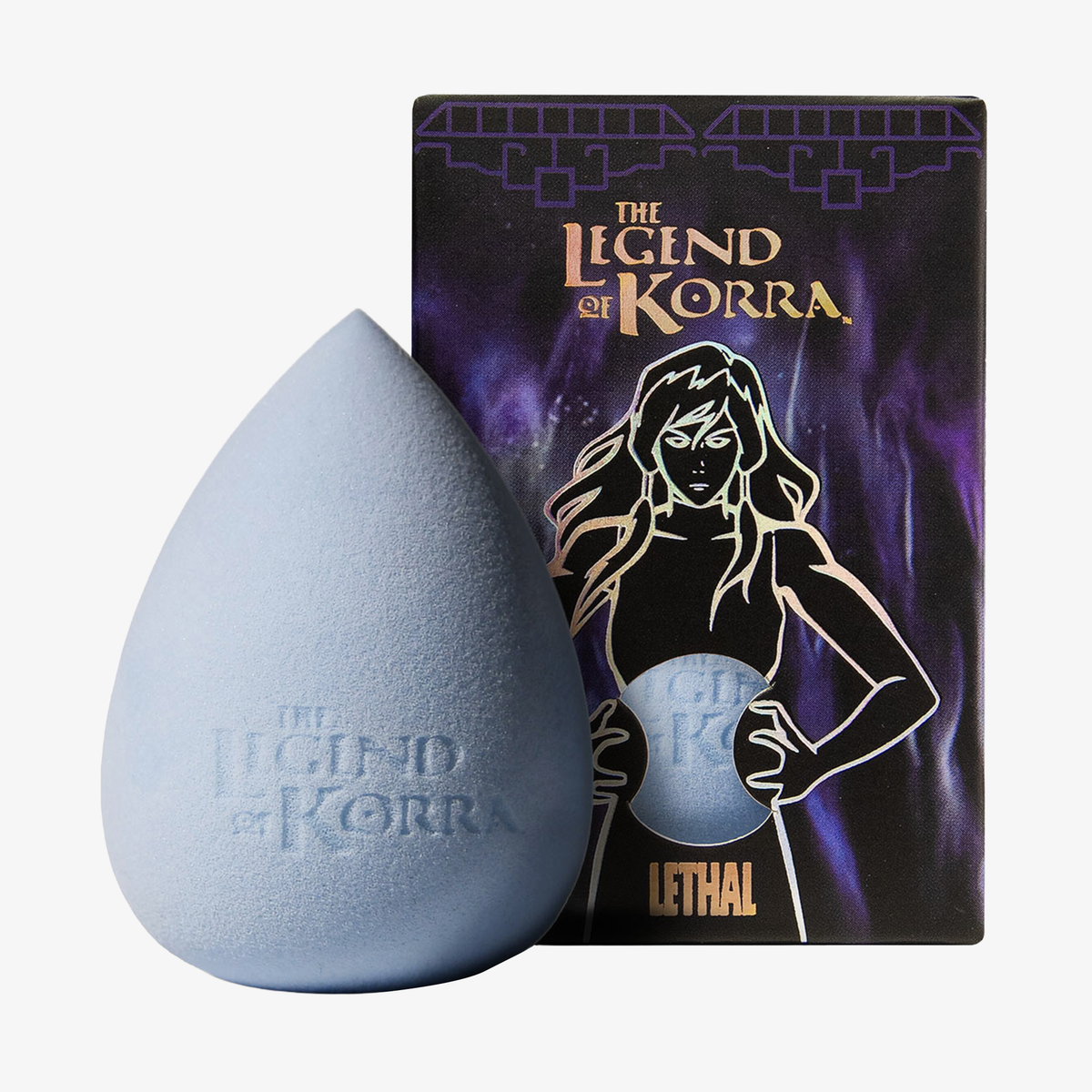 Ein farbwechselnder Schwamm der Marke „Lethal Cosmetics“ aus der Serie „Legend of Korra: Spirit World“ liegt neben einer Schachtel, auf der eine Frau abgebildet ist, die eine leuchtende Kugel in der Hand hält.