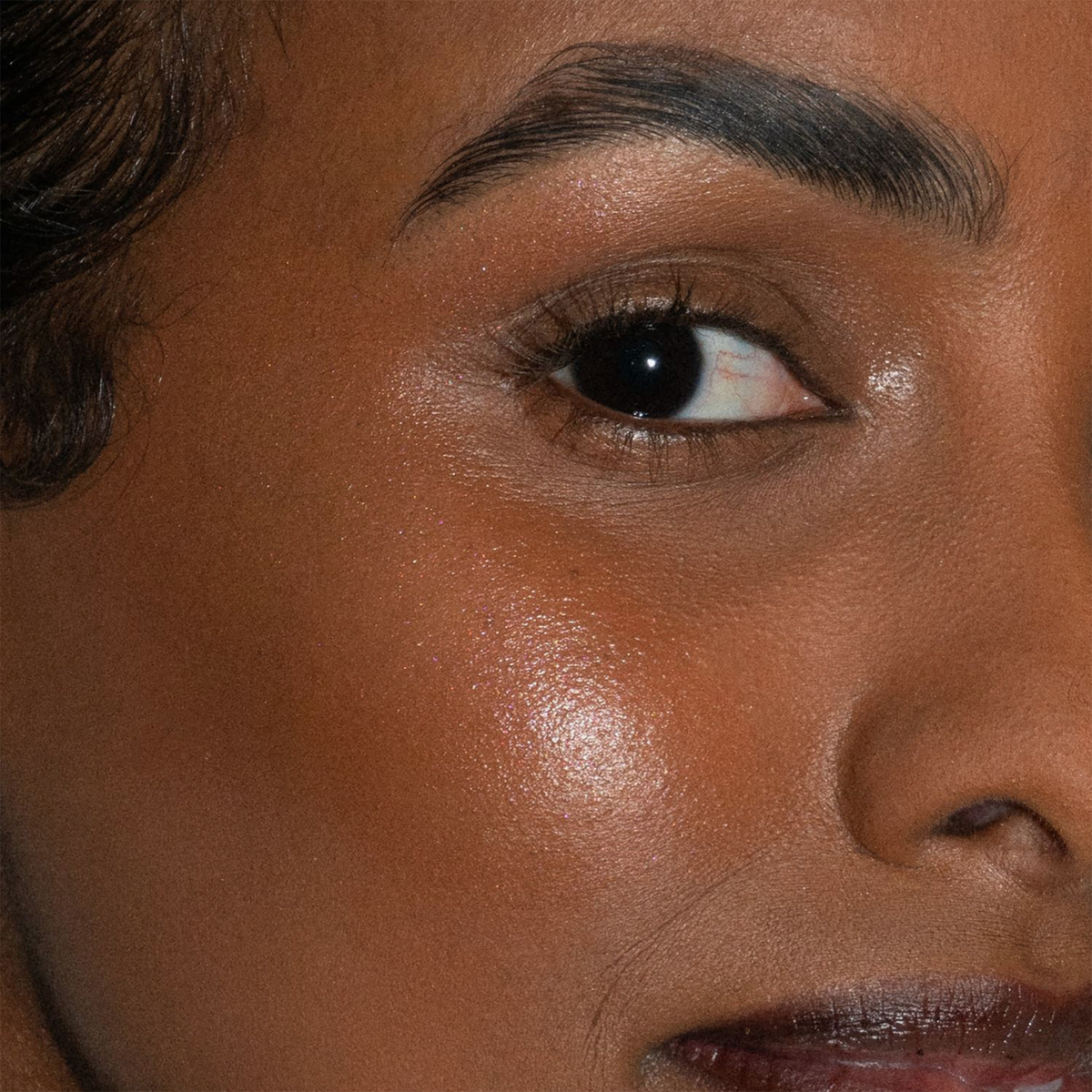 Nahaufnahme von Auge und Augenbraue einer Frau, die mit LH Cosmetics Artistick Highlighter glatte, strahlende Haut hervorhebt.