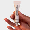 Eine Hand drückt den LH Cosmetics Till The End Eyeshadow Primer auf eine Fingerspitze vor einem neutralen Hintergrund.