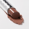 Der braune Lippenstift Mesauda Milano Hydramorphosis im Metallic-Etui schmilzt an der Spitze auf einer weißen Oberfläche.