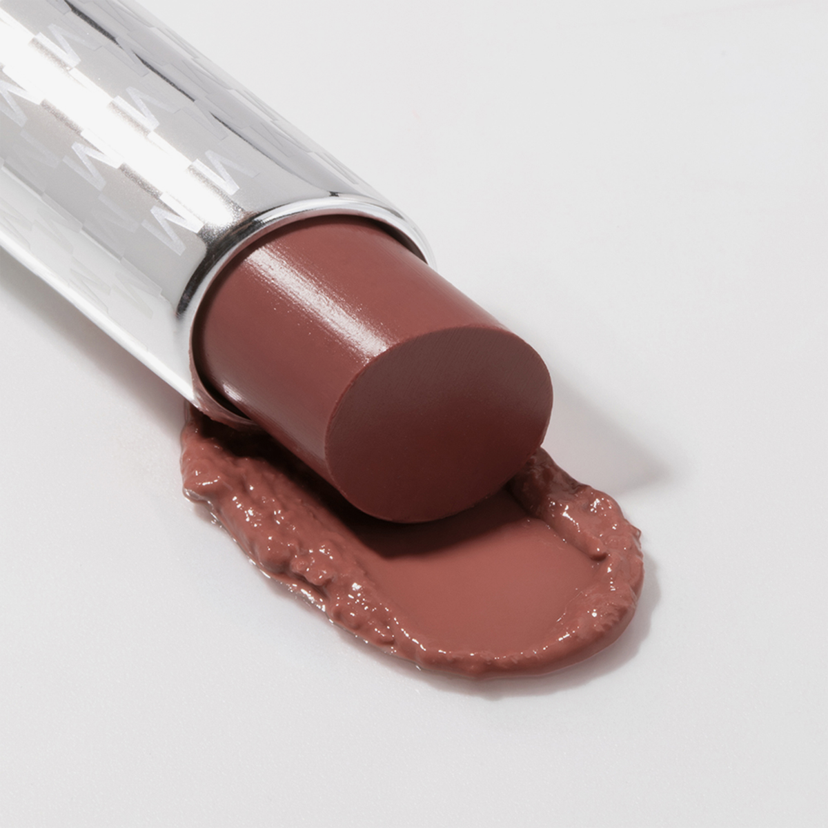 Der lilafarbene Lippenstift Mesauda Milano Hydramorphosis in einem silbernen Etui liegt auf einer weißen Fläche, seine Spitze ist teilweise geschmolzen.