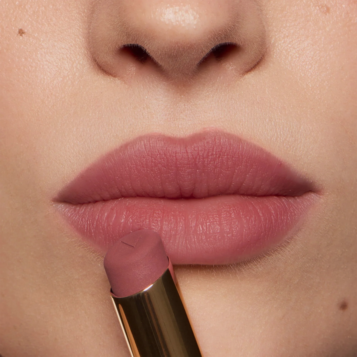 Nahaufnahme von Lippen mit rosigem Mauve-Lippenstift und weich verblendetem Ombré-Effekt. Ein Lippenstift wird vor den Lippen gehalten.