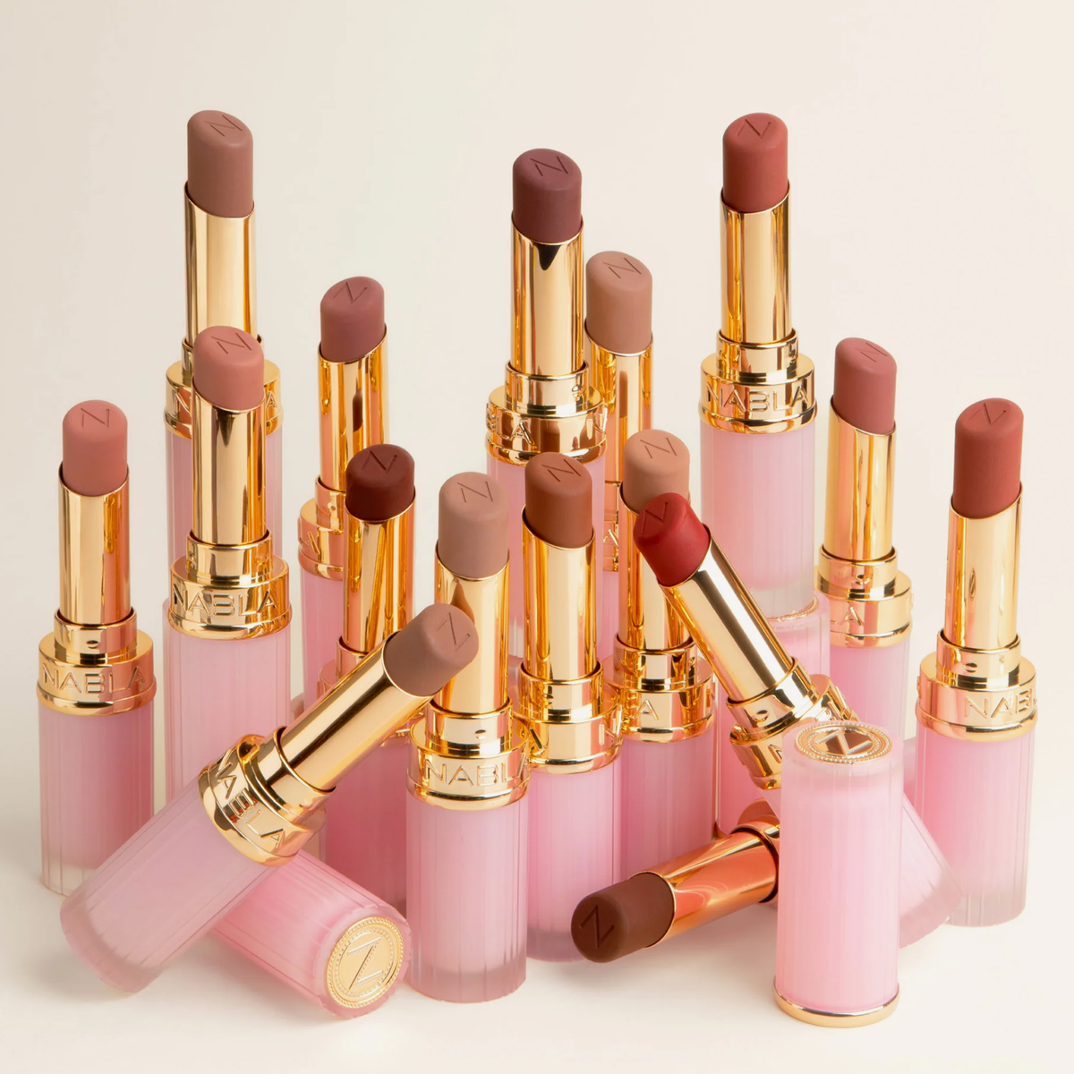 Mehrere geöffnete Nabla Beyond Blurry Lippenstifte in verschiedenen Nude-, Rosé- und Rottönen mit rosafarbenen Hüllen und goldenen Details.