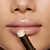 Nahaufnahme von glänzenden Lippen, als eine Person den Beyond Jelly Lipstick Pearlescent von NABLA Cosmetics aus einer goldenen Tube aufträgt.