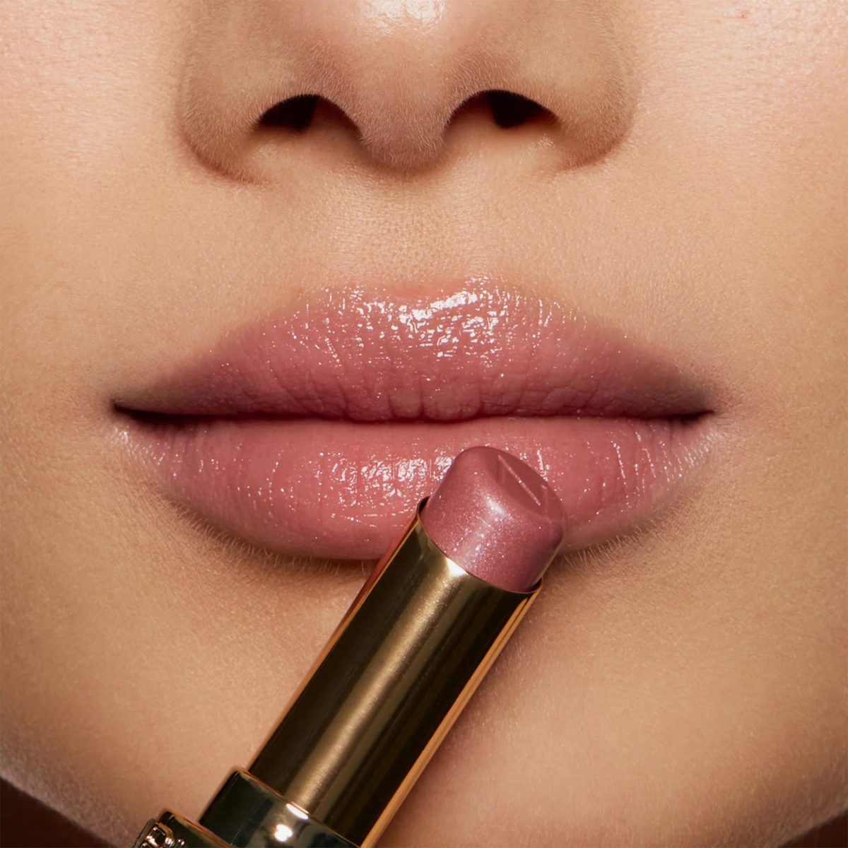 Nahaufnahme von glänzenden Lippen beim Auftragen des Beyond Jelly Lipstick Pearlescent von NABLA Cosmetics aus einer goldenen Tube.