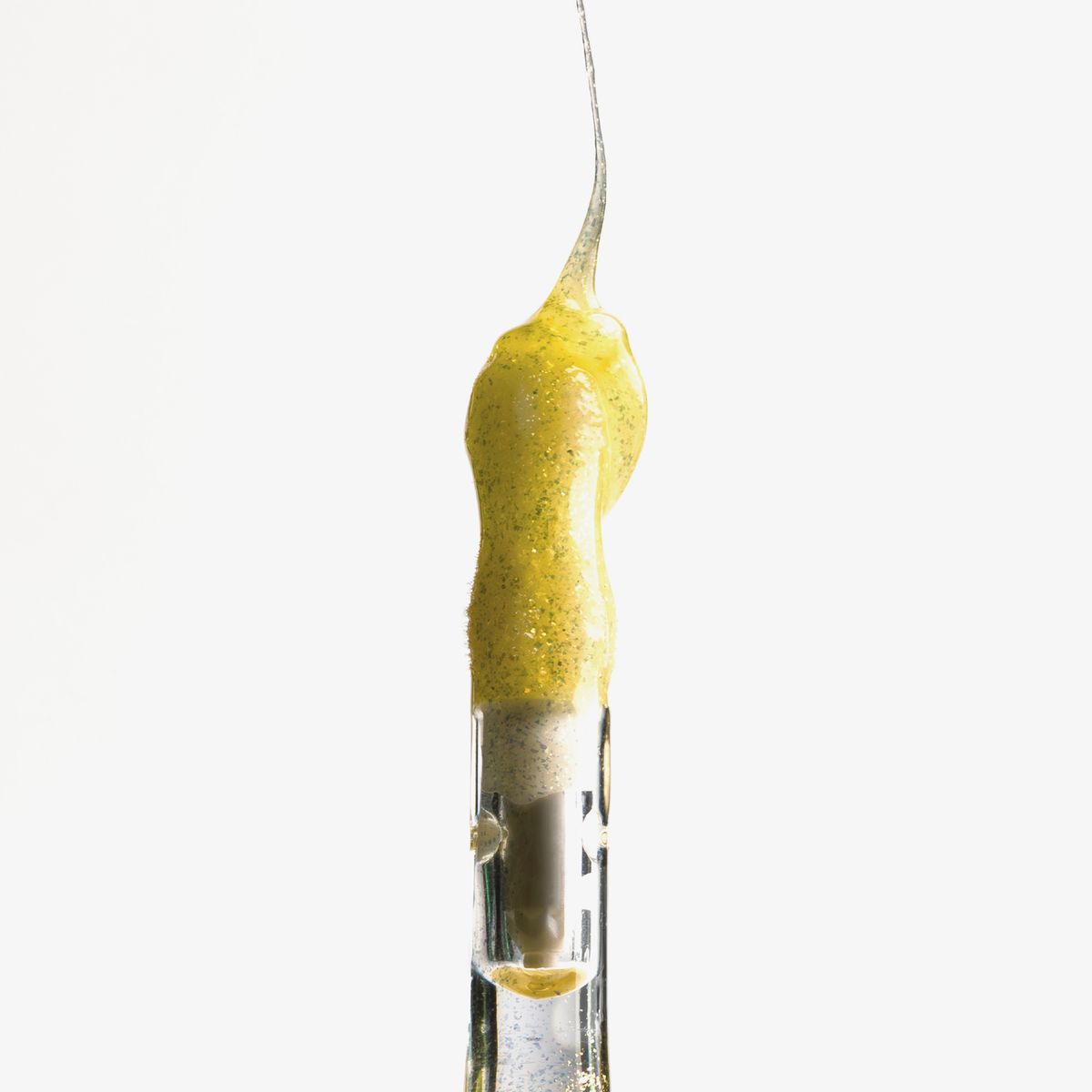 Lip Candy Oil von NABLA Cosmetics fließt auf den gleben Applikator der sich golden und glänzend vor einem weißen Hintergrund abhebt.