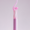 Aus dem „Lip Candy Oil“ von NABLA Cosmetics erhebt sich ein rosafarbener, glänzender Wirbel, der mit seiner eleganten rosa Tube vor einem blassen Hintergrund harmoniert.
