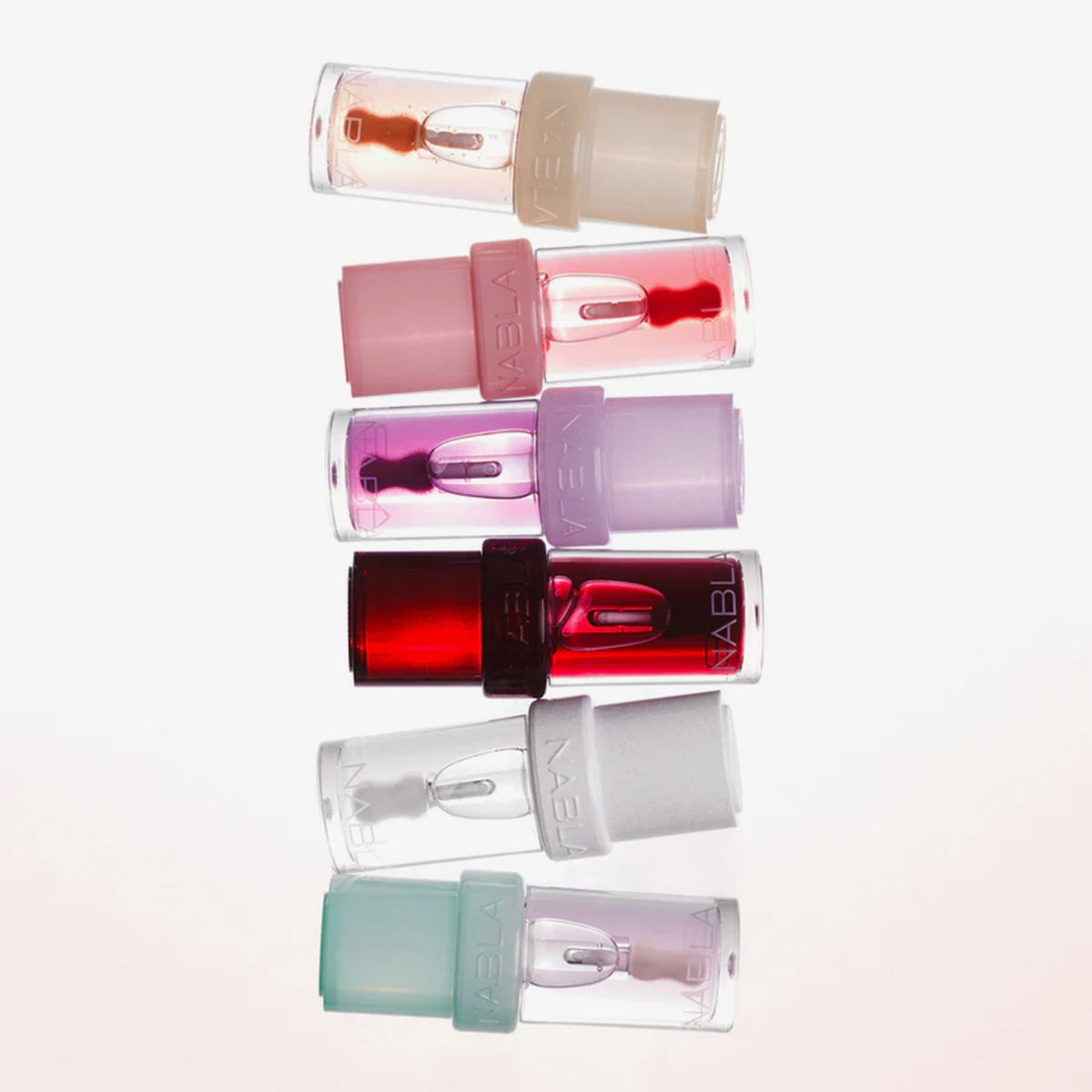 Sechs NABLA Lip Candy Oils in bunten Verpackungen liegen nebeneinander, jede mit transparenter Hülle und farbigem Deckel.