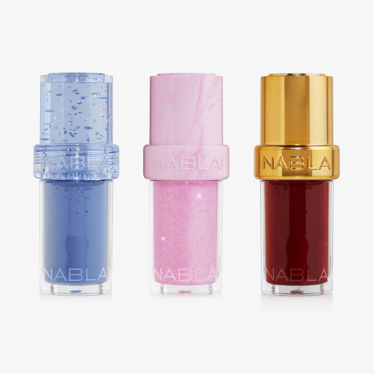 Drei NABLA Cosmetics Lip Candy Oil - Sweet Kiss Kit Glosse in Blau, Glitter Pink und Gold Deep Red, aufrecht nebeneinander stehend.