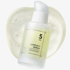 Eine gefrostete Flasche des Numbuzin No.5 Goodbye Blemish Serum ruht auf einer durchsichtigen Serumschicht.