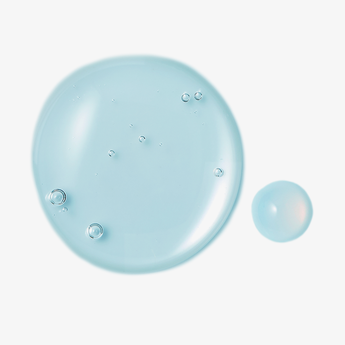 Zwei Tropfen des „Numbuzin No. 6 Deep Sleep Mask Serum“, hellblau mit Bläschen, auf weißem Hintergrund.