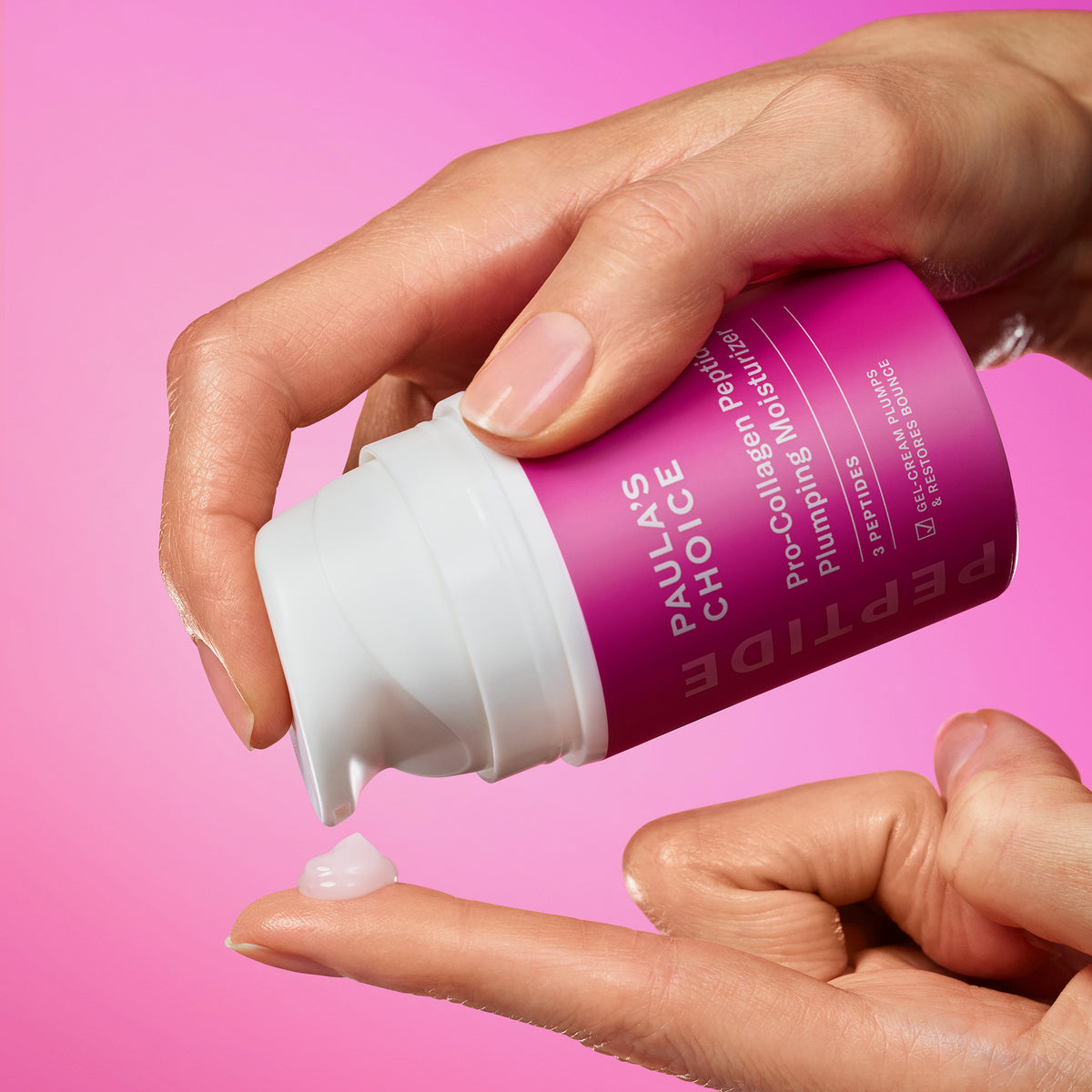 Eine Hand verteilt Paula's Choice Pro-Collagen Peptide Plumping Feuchtigkeitscreme auf eine Fingerspitze vor einem rosa Hintergrund.