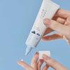 Runde Tube der Round Lab 1025 Dokdo Eye Cream mit hellblauem Design wird auf einen Finger aufgetragen.