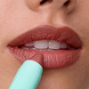 Eine Nahaufnahme einer Person, die sich den SWEED Le Lipstick in der Farbe Mauve aus einer hellblauen Tube auf die Lippen aufträgt.