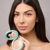 Eine Frau mit langen, dunklen Haaren hält den „SWEED The Highlighter“ nahe an ihr Gesicht und präsentiert damit ein klares, natürliches Make-up.