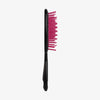 Die UNbrush Detangling Hair Brush hat rosa Borsten und einen schwarzen Griff, der aufrecht vor einem schlichten weißen Hintergrund steht.