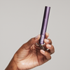 Vor einem einfarbigen Hintergrund hält eine Hand eine violette Tube mit der Aufschrift „XLASH Xbrow Sensitive Eyebrow Serum“ in der Hand.