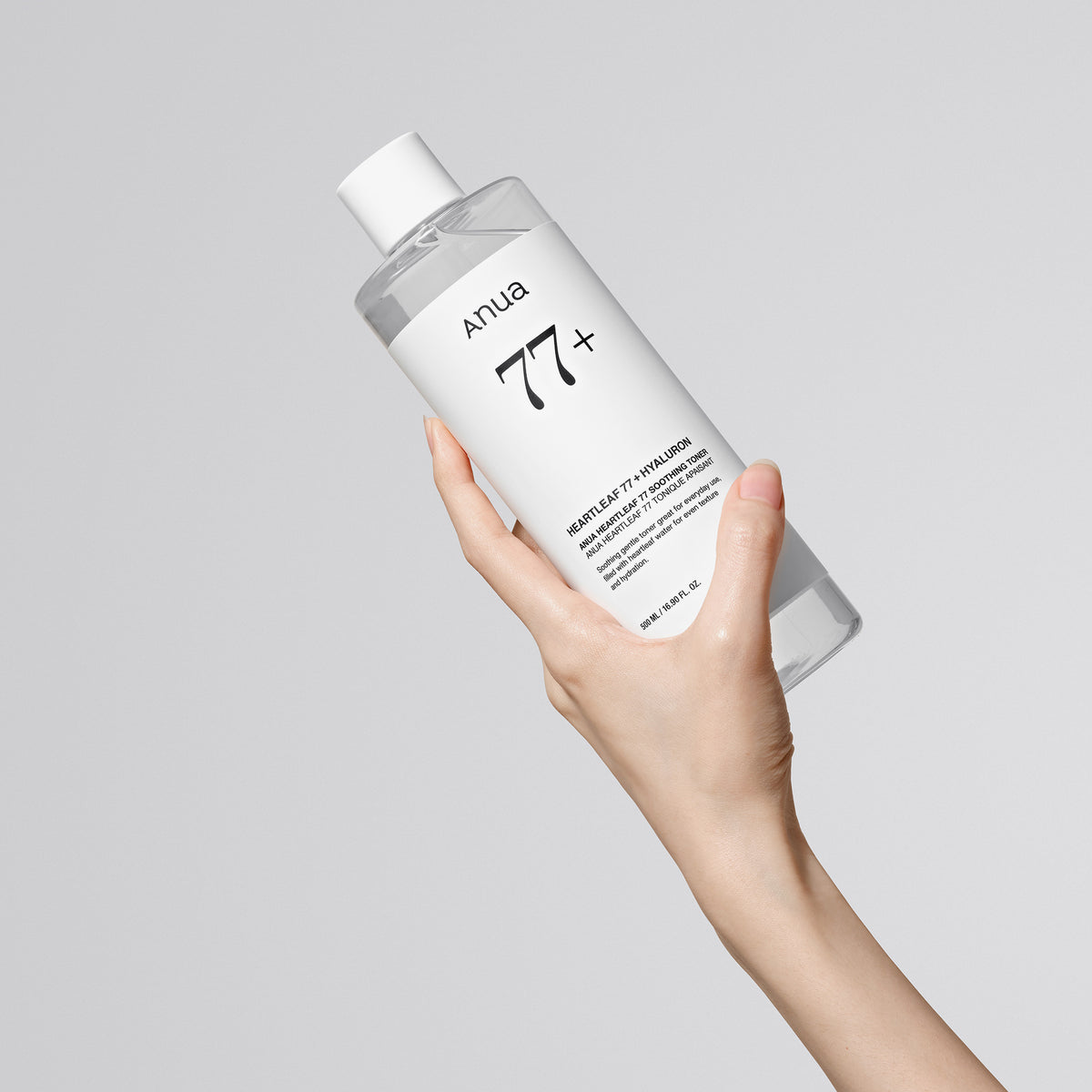 Eine Hand hält eine durchsichtige Flasche Heartleaf 77 % Soothing Toner vor einem schlichten hellgrauen Hintergrund.