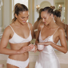 Zwei blonde Frauen in weißer Wäsche verwenden Bali Body Body Scrub in einem edlen Badezimmer.