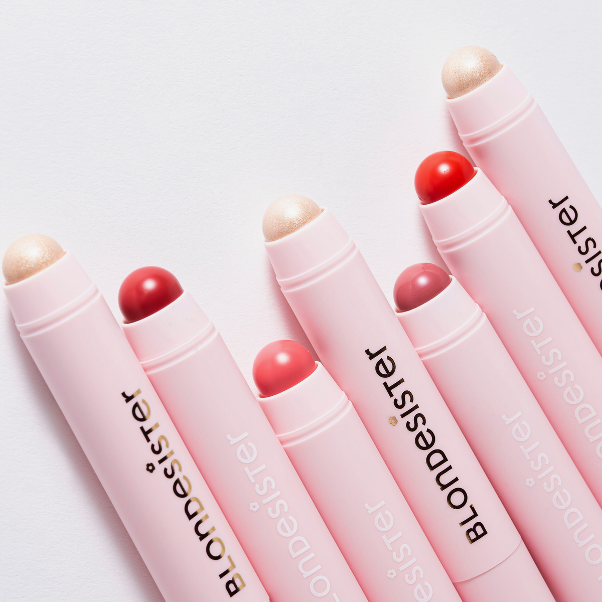 Sechs rosafarbene BLONDESISTER 2-IN-1-Stifte „IT’S UP TO YOU – LIP OR CHEEK“ mit verschiedenen Lippenstift- und Highlighter-Spitzen auf weißem Hintergrund.