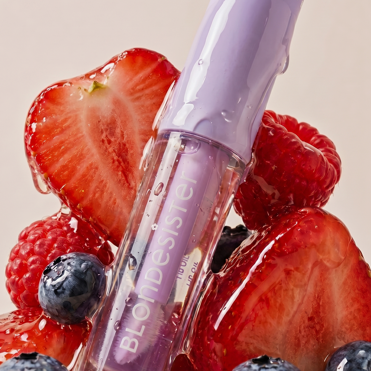 Eine Tube „BLONDESISTER 3 IN 1 CUTE LIPPY LIP OIL“, umgeben von Erdbeeren, Himbeeren, Heidelbeeren und glitzerndem Sirup.