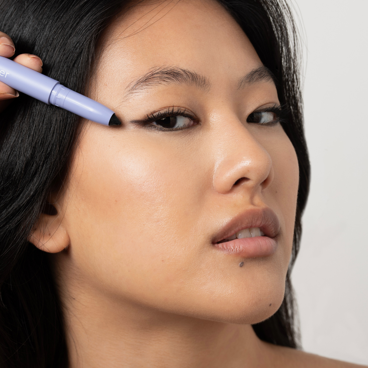 Jemand verwendet „BLONDESISTER 3 IN 1 EYES ON ME“, um schwarzen Eyeliner auf das obere Augenlid nahe dem äußeren Augenwinkel aufzutragen.