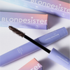 Eine lavendelfarbene 4-in-1-CLICK-&-TURN-Mascara-Tube mit Applikator, im Hintergrund pastellfarbene BLONDESISTER-Verpackungen.