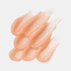 Pillow Plush Peptide Lip Mask 010 ist ein pfirsichfarbenes Gel, das in überlappenden, gewellten Linien auf weißem Grund aufgetragen ist.