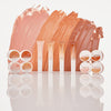 Eine Reihe von Catrice Cosmetics Under Eye Brightener Liquid in verschiedenen Farbnuancen, die vor den passenden Farbmustern angeordnet sind.