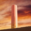 Der Catrice Cosmetics MIDNIGHT SUN Jelly Glow Stick steht aufrecht mit einem dramatischen Sonnenuntergangshimmel im Hintergrund.
