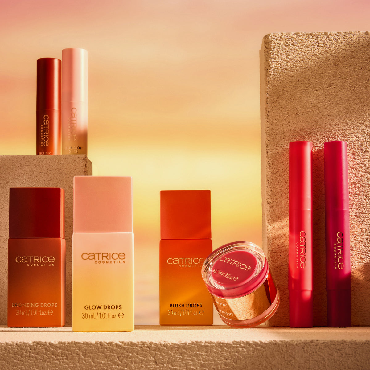 Die Catrice Cosmetics MIDNIGHT SUN Collection ist auf beigen Blöcken vor einem warmen, sonnenuntergangsfarbenen Hintergrund abgebildet.