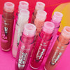 Neun Tuben Essence Extreme Shine Volume Lipgloss in verschiedenen Rosa- und Nude-Tönen auf einem leuchtenden Hintergrund.