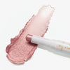 Schimmernder pinker Glitterstick von essence, auf einer weißen Fläche aufgetragen und danebenliegend.