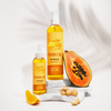 Zwei Flaschen Hair Syrup Vitamin C Me werden mit Papaya, Orangenscheiben und Macadamianüssen auf weißen Steinen präsentiert.