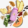 Violette BLOATamin-Flasche, umgeben von Ingwer, Ananas, Papaya, Kräutern und Gewürzen.