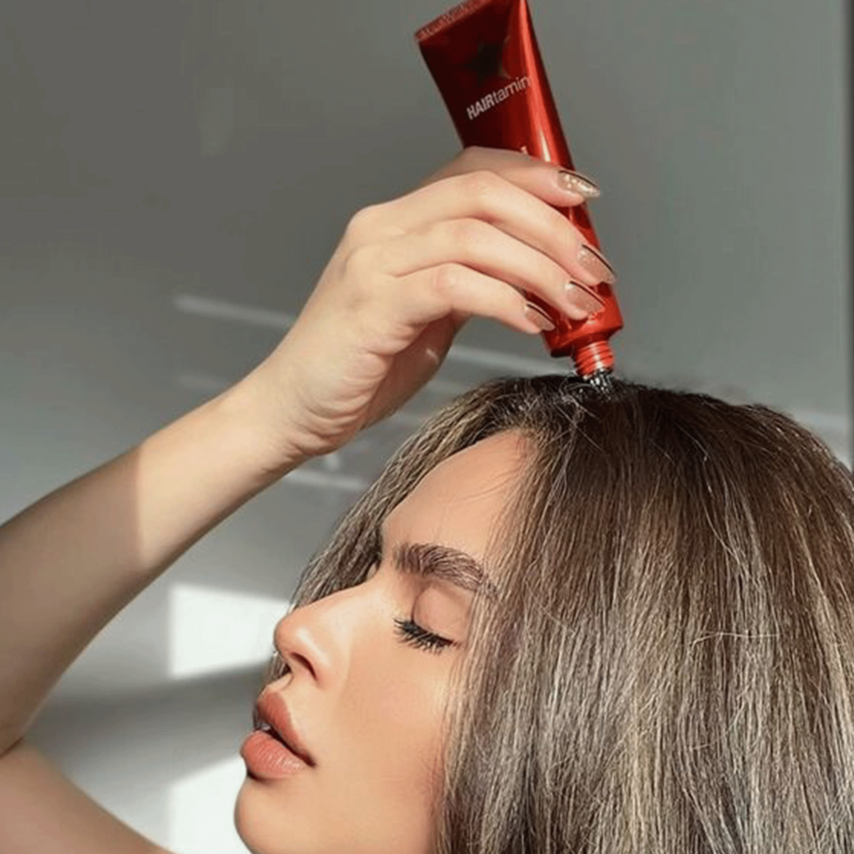 Frau trägt ein rotes Hairtamin Scalp Serum mit Applikatorspitze direkt auf den Haaransatz auf, Anwendung in Nahaufnahme.